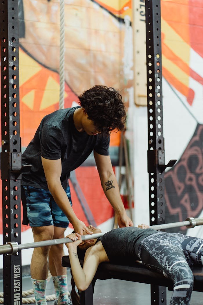 gallery-3 A personal trainer helps a client during a bench press session in a modern gym.