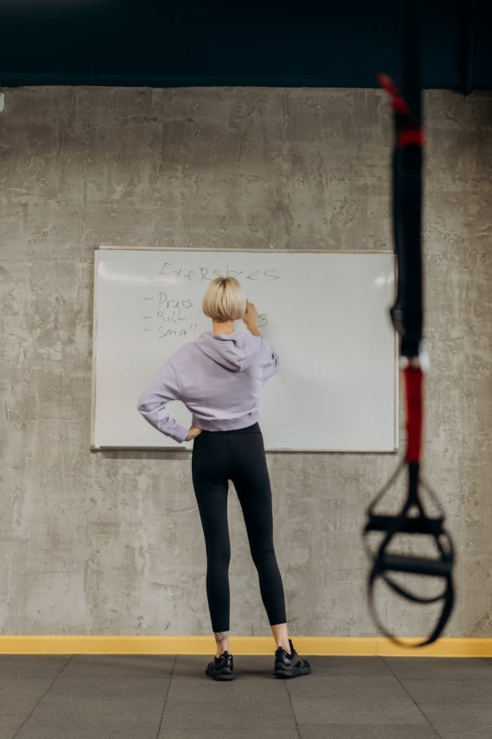 Female fitness instructor writing exercises on a whiteboard in a gym.